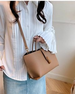 Detail view of brown lychee grain leather texture and gold hardware on tote bag