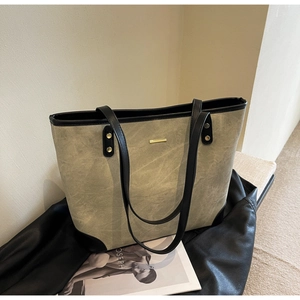 Detail of olive green tote bag featuring black leather straps and gold metal bar accents