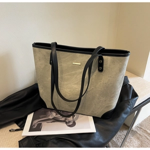 Close-up of grey-green matte tote bag with black leather straps and gold metal accents