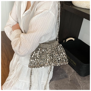 Detailed view of silver sequin woven bag with metallic chain strap on a model