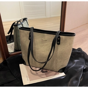 Detail view of large tote bag with contrast black trim and gold metal accent on green fabric