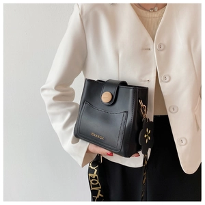 Sac seau noir en cuir avec boucle en bois et bandoulière fleurie tenu par un mannequin