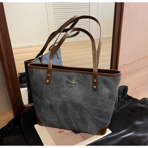 Detailed close-up of stone-textured tote bag with brown trim and metallic logo detail