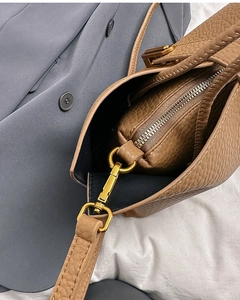Close-up of brown lychee grain leather handbag featuring gold hardware and inner pouch