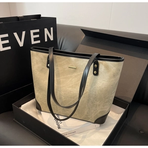 Detail of olive green tote bag featuring black leather trim and golden metal logo bar