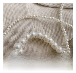 Close-up of woven pearl mini handbag with silver rings on beige textured background