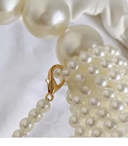 Detail of elegant pearl strap with golden lobster clasp on a white fabric background