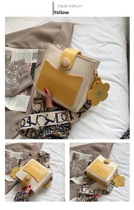 Détail d'un sac bandoulière contrasté avec boucle en bois et breloque fleurie