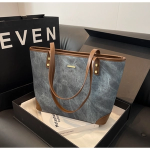 Detail of grey washed denim tote bag with brown leather handles and golden metal trim