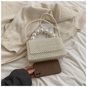 Detail of handmade white pearl woven handbag showing size capacity next to a smartphone