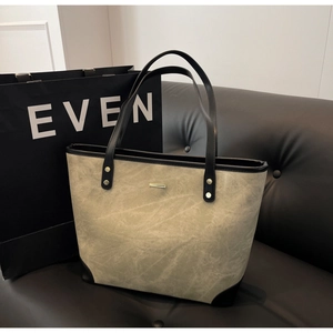 Detail of grey-green tote bag with black handles and gold hardware on leather sofa