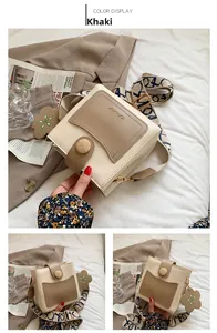 Détail du sac seau kaki avec boucle en bois et large bandoulière sur lit blanc
