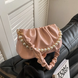 Pink pleated dumpling bag with pearl strap and golden hardware on a leather surface