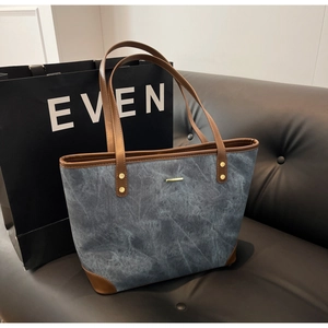 Detail of blue denim texture tote bag with brown leather handles and gold metal accents