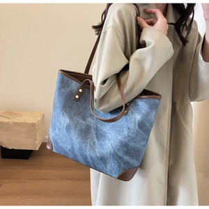 Side view of large blue canvas tote bag with brown leather trim carried by a model