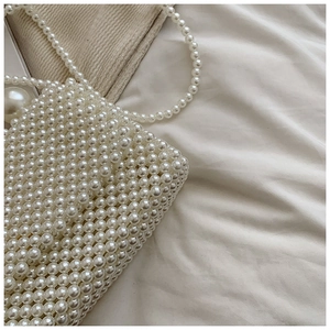 Detail of white pearl woven handbag with matching shoulder strap on soft fabric background
