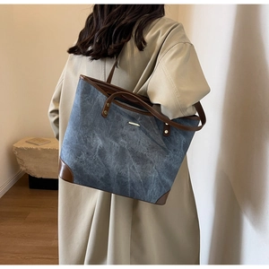 Detail view of denim tote bag with brown leather trim and metal logo plate on shoulder