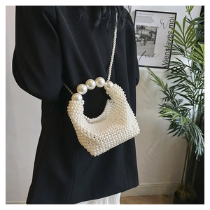 Detail of handcrafted cream pearl woven handbag with large pearl handle on a model shoulder