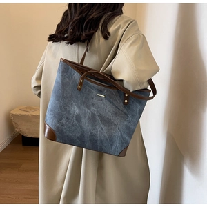 Detail of blue denim tote bag with brown leather handles and reinforced corners