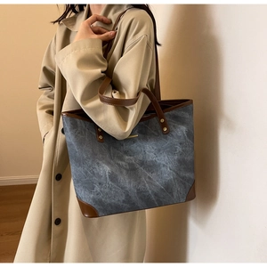 Detail of blue denim tote bag with brown leather handles and gold rivet accents