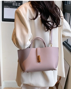 Close-up of lilac lychee grain leather bucket bag with gold metal clasp on white suit