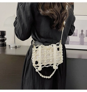 Detail of white pearl woven bucket bag with long strap on a black pleated dress