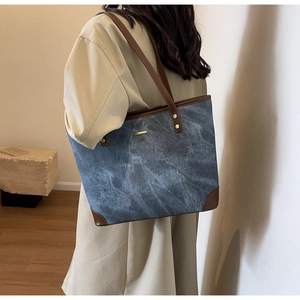 Detail of blue denim tote bag with brown leather trim held by a model in a modern room