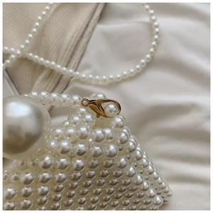 Detailed close-up of handmade white pearl woven bag with golden lobster clasp and large bead