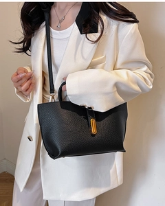 Close-up of black lychee grain leather tote bag featuring a gold metal oval clasp detail