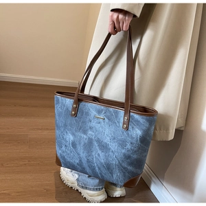 Blue denim tote bag with brown leather handles held by model in home setting