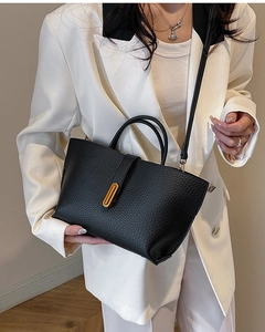 Close-up of black lychee grain tote bag with gold oval lock on white blazer model