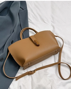 Detail of brown lychee leather handbag with golden twist lock on grey blazer background
