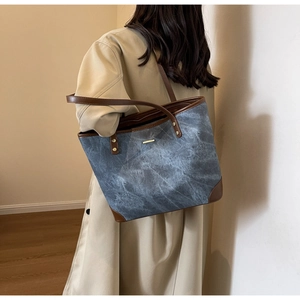 Detail of blue textured tote bag with brown leather straps and metal rivets on shoulder