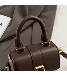 Détail de la poignée marron foncé avec attaches métalliques dorées sur le sac à main
