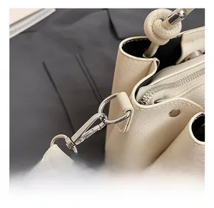 Gedetailleerde close-up van zilveren metalen haken en lychee-nerf leer op de crème tas