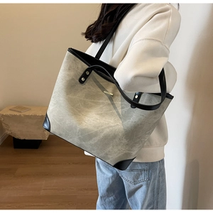 Detailed shot of stone grey tote bag with black leather straps and gold metal accent