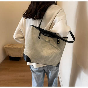 Detail of grey marble textured tote bag with black leather reinforced corners and gold accent