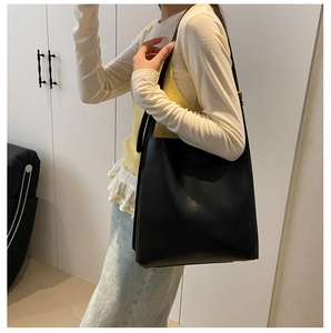 Detail of a large black matte leather tote bag worn by a model for daily commuting