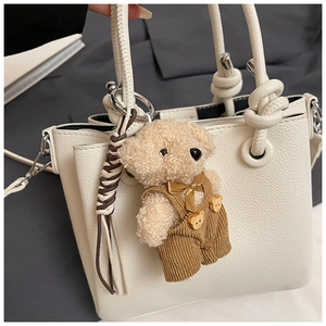 Close-up of white pebble leather bucket bag with a cute teddy bear charm and knot handle