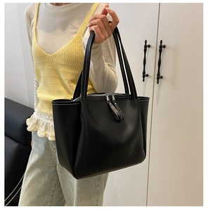 Close-up of black leather tote bag featuring contrast white stitching and dual zipper closure