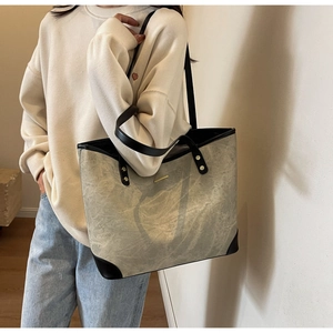 Detail of grey-green tote bag with black leather handles and gold metal accent