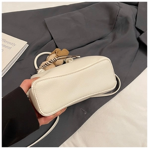 Detail of off-white lychee texture bucket bag with cute brown plush bear charm accessory