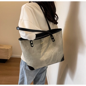 Detail of grey textured tote bag with black trim and elegant gold hardware accent
