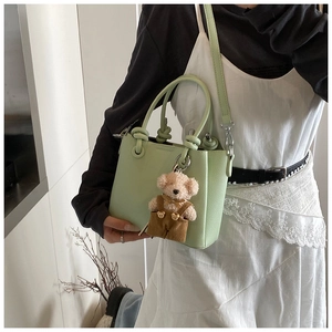 Detail van de muntgroene emmertas met gedraaid handvat en teddybeer-hanger op witte jurk