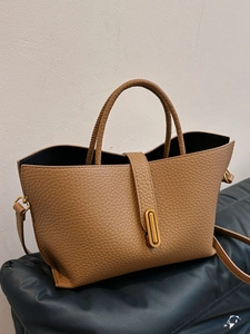 Brown lychee leather tote bag with gold oval twist lock on navy blue cushion