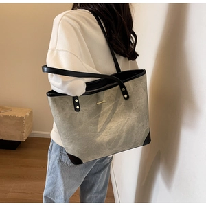 Detail of grey-green tote bag with black leather edges and gold metal rivet accents