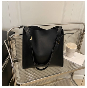 Detail of minimalist black tote bag with adjustable straps and golden metal buckles