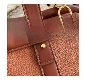 Macro view of brown lychee grain leather handbag with gold buckle and neat stitching