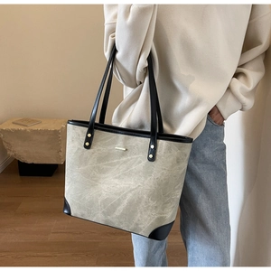 Close-up of stone-textured tote bag with black leather straps and gold metal studs