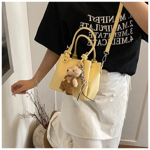 Detailed view of yellow bucket bag with brown plush bear charm and adjustable shoulder strap